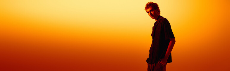 Stylish young man enjoys a moment at sunset with a vibrant orange backdrop