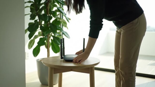 Modern living: Woman's hands placing and adjusting a black Wi-Fi router on a wooden table in a bright home or office setting