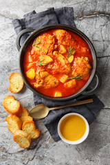 Chicken Bouillabaisse soup in a rich tomato-vegetable broth served with toasted baguette and rouille sauce, close-up in a pan on the table. Vertical top view from above