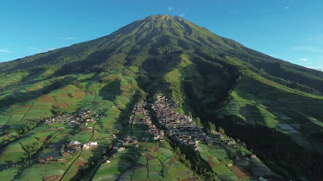 Aerial view of Nepal Van Java village nestled amidst vibrant green terraced fields, under the shadow of a majestic mountain, Magelang, Central Java, Indonesia.