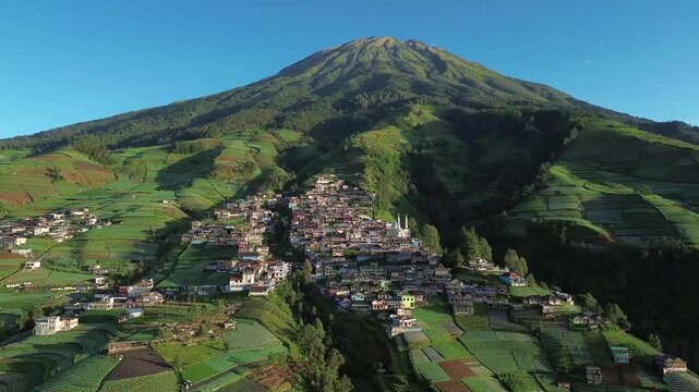 Aerial view of Nepal Van Java village nestled on verdant slopes, a mosaic of terraced fields climbing to the majestic mountain peak, Magelang, Central Java, Indonesia.
