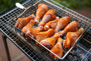 Raw seasoned chicken drumsticks arranged in a grilling basket over hot coals on a barbecue