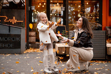 mom and daughter walk with yellow leaves in autumn, throwing them, making leaf fall in a cafe, hugging, autumn walk, happy family, maternal love