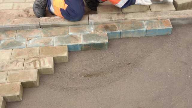 an experienced construction worker in work gloves lays paving stones