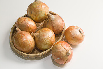 stacked raw onion with skins on bamboo basket.