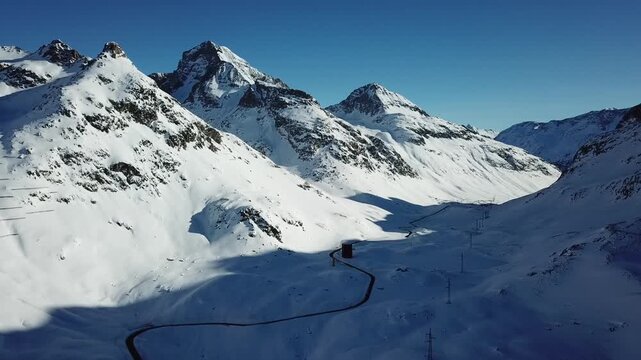 Aerial view of the snow covered mountains contrasting with the dark winding road at Julier Pass, Grisons, Switzerland.