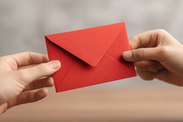 Fototapeta premium Two hands exchanging red envelope, symbolizing gift or message. background is blurred, focusing on hands and envelope, conveying sense of anticipation and connection