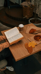 Cozy autumn scene with coffee, book, and pastries on a wooden table.