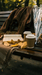 Autumn scene with coffee, a book, and fall leaves on a park bench.