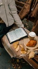 Reading the Bible with coffee and croissant on a park bench in autumn