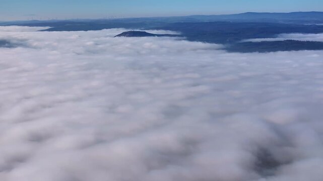 Aerial view of rolling hills emerging from a sea of fluffy white clouds, creating a serene and ethereal landscape, Eichenzell, Hessen, Germany.