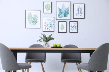 Stylish room interior with modern table, chairs and paintings of tropical leaves. Idea for design
