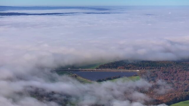 Aerial view of the lake and highway cutting through the landscape, shrouded in a blanket of fog, with vibrant trees, Eichenzell, Hessen, Germany.