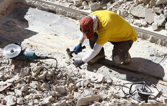 Obrero con martillo, cincel cortafr&iacute;o y radial golpeando y picando piedra en obra reforma de suelo en patio