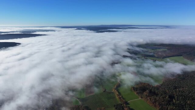 Aerial view of the clouds blanketting the landscape, partially covering green fields and forests in a beautiful spectacle of nature, Eichenzell, Hessen, Germany.