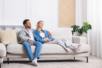 Fototapeta premium Couple with air conditioner remote control on sofa at home