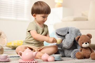 Cute little boy playing tea party with his toys indoors
