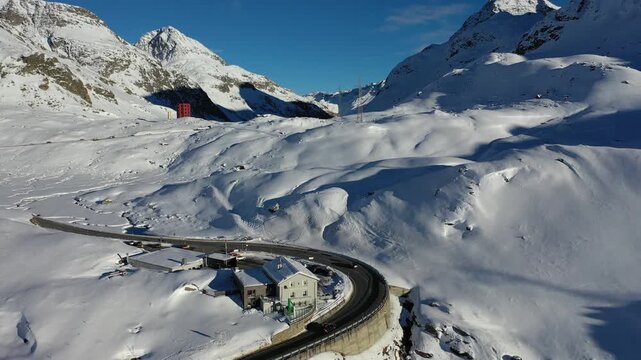 Aerial view of the snow blanketed Julierpass mountain range and winding road contrasting with the blue sky above, Julierpass, Grisons, Switzerland.