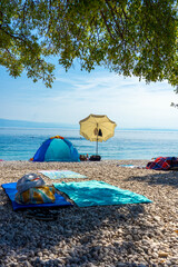 Pebble beach with umbrellas, towels and tent by the calm Adriatic Sea in Croatia