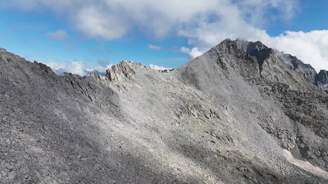 Aerial view of rugged, rocky mountain peaks under a blue sky with scattered clouds, showcasing the stark beauty of the alpine landscape, Brescia, BS, Italia.