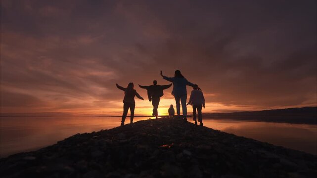 Group of happy young people running at the rocky spit of a high-mountain lake in the Gobi Desert, Mongolia on beautiful summer sunset. The concept of travel, youth, and shared adventures in nature