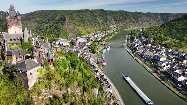 Aerial footage of Moselle River in Germany with cargo ships and tourist boats, town of Cochem and Reichsburg Cochem castle overlooking the river valley.
