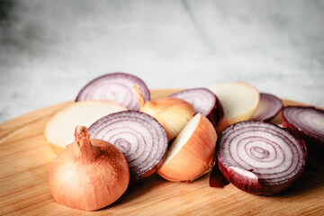 Playful arrangement of red and yellow onion parts, slices, and skins on wooden cutting board. Conceptual still life with natural textures and artistic imperfection
