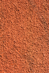 A vertical close-up shot of a rough, terra cotta colored wall with a stucco-like texture