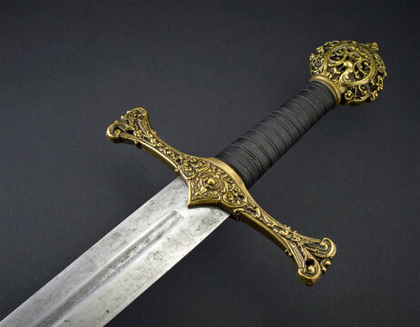 Ornate medieval broadsword with a beautifully crafted golden hilt, black wrapped grip, and a weathered steel blade on a dark background