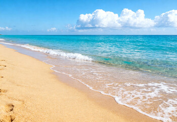 Clear blue sky, golden sand, gentle waves, sunny day.