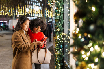 Diverse women friends using smartphone shopping at christmas