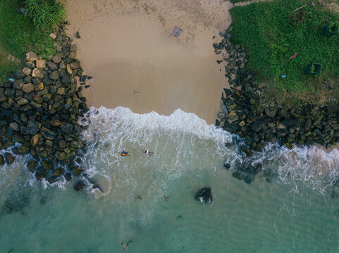 Aerial view of the meeting point of the ocean and the sandy beach, framed by rocky outcrops covered in green vegetation, Welligama, Sri Lanka.