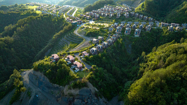 Aerial view of modern villas nestled amongst the verdant, rolling hillsides, with winding roads and sun-drenched slopes, creating a serene landscape, Zhangjiajie, Hunan, China.