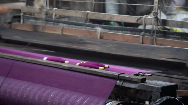 Automated textile weaving loom machine processing purple fabric in Indian factory