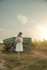 Young woman in white dress walking with daisies at sunset