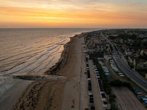 Aerial view of the beach, with beach huts and a coastal road running parallel under a vibrant sunset sky, Berni&Atilde;&uml;res-sur-Mer, Normandy, France.