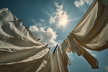 White laundry hanging on a clothesline against a bright blue sky with fluffy clouds and sun rays shining down, creating a serene and peaceful outdoor atmosphere