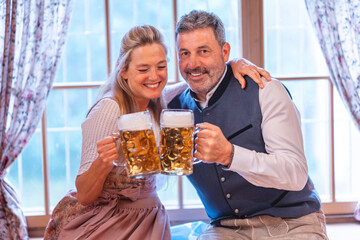 Cheerful Bavarian couple in dirndl and lederhosen clinking beer mugs symbol of Oktoberfest celebration and German tradition