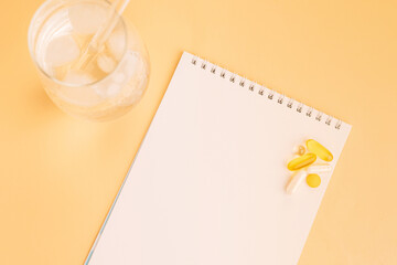 Iced water glass and vitamins on pastel desk with notepad. High quality photo