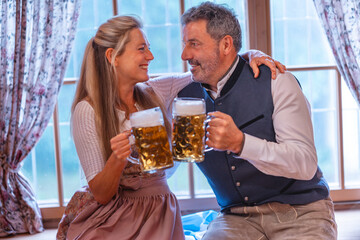 Traditional Bavarian couple in dirndl and lederhosen clinking beer mugs enjoying Oktoberfest culture and festive atmosphere