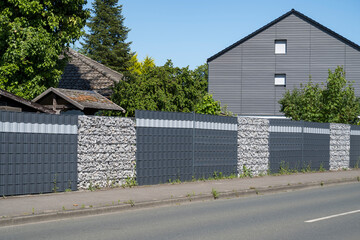 Modern metal fence with gabions and anthracite blinds in front of house