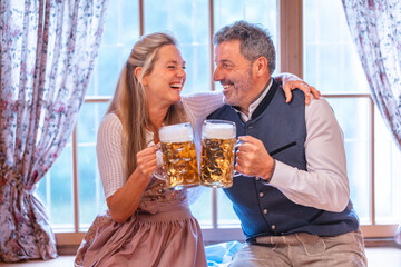 Smiling Bavarian couple in folk dress clinking beer mugs Oktoberfest joy symbol of German tradition folklore and celebration