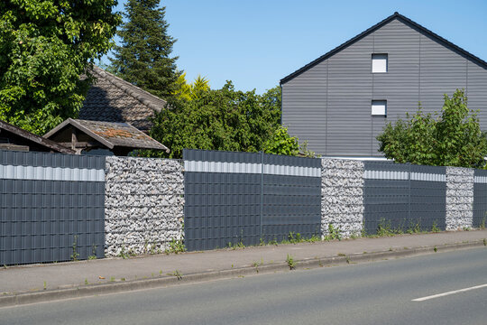 Modern metal fence with gabions and anthracite blinds in front of house