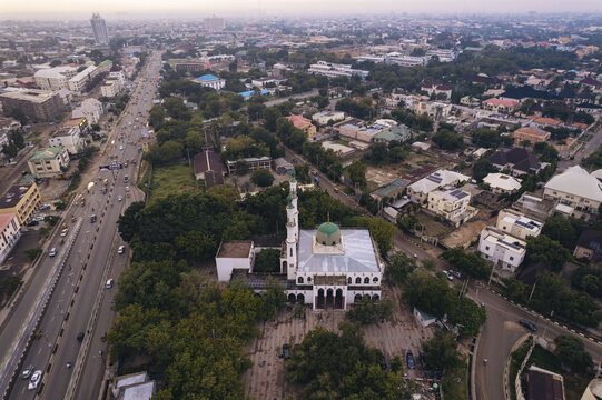Aerial view of the serene mosque's white facade under a green dome, amidst lush trees and bustling roads, Zaria Road, Kano, Kano, Nigeria.