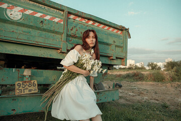 Thoughtful young woman with daisies sitting by farm trailer.Retro grain effect
