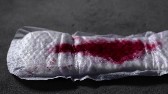Bloody female discharge on a menstrual pad.
Close-up of a sanitary pad on a gray surface.
Women's health and hygiene.
Women's, health, blood, menstruation, cycle