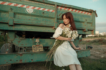 Thoughtful young woman with daisies sitting by farm trailer.Retro grain effect