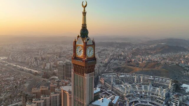 drone footage of Mecca, Saudi Arabia, filmed at sunset. The video captures the vast urban landscape with residential buildings, modern towers, and surrounding mountains bathed in golden hour light