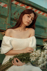 Thoughtful young woman with daisies sitting by farm trailer.Retro grain effect