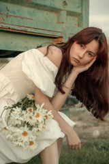 Thoughtful young woman with daisies sitting by farm trailer.Retro grain effect